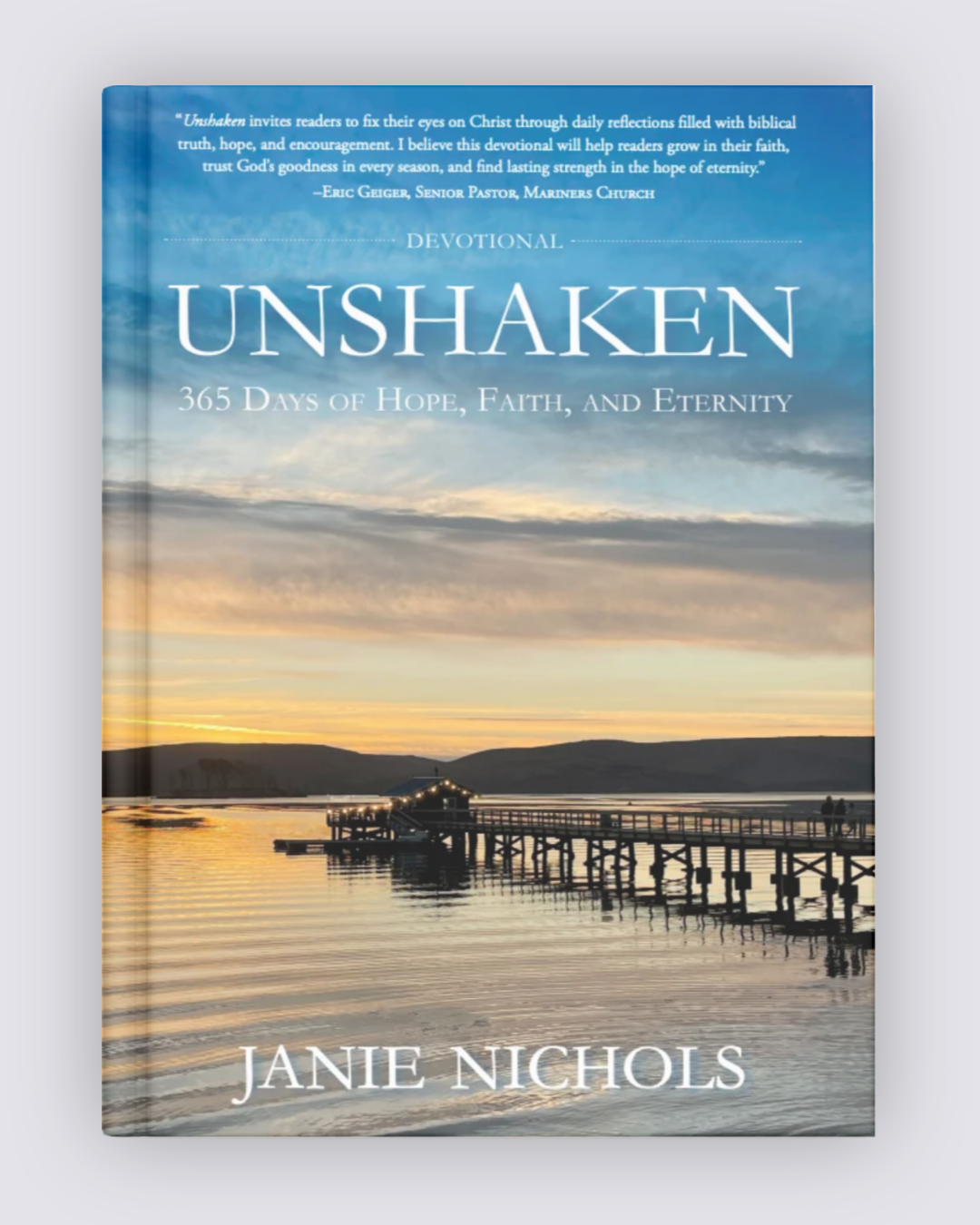 A hardcover book titled 'Unshaken: 365 Days of Hope, Faith, and Eternity' by Janie Nichols, featuring a scenic sunset over water with a pier on the cover, set against a plain light gray background.
